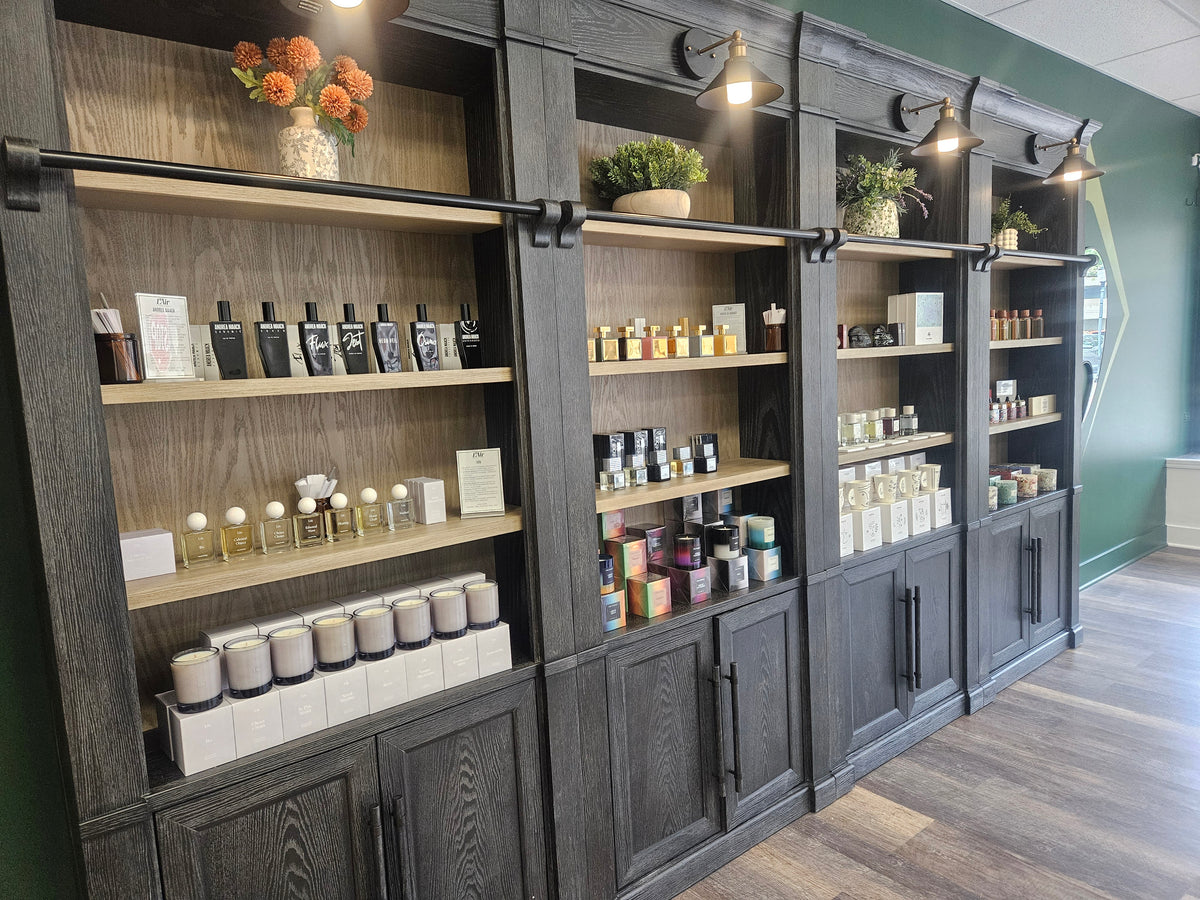 The L'Air retail display wall with dark wood cabinetry and open shelves holding indie and niche fragrances and candles, photographed in a store interior with wood flooring and green walls.
