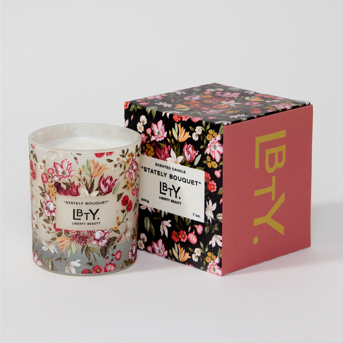 Stately Bouquet candle by Liberty London. Its notes are blackberry, pomegranate seeds, saffron, stone fruits, star anise, cashmere woods, sugared patchouli, musks. It is a white candle contained by a semi-opaque glass jar painted with pink and red flowers. It sits beside a black and red box, also covered with pink and red flowers.